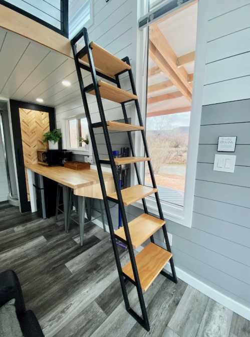 A modern interior featuring a black metal ladder with wooden steps leading to a loft area, beside a kitchen space.